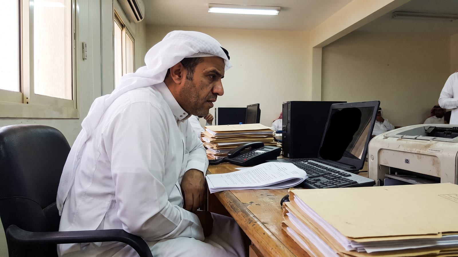 A business owner in a Riyadh office reviews an AI agency proposal at a messy desk, looking uncertain.