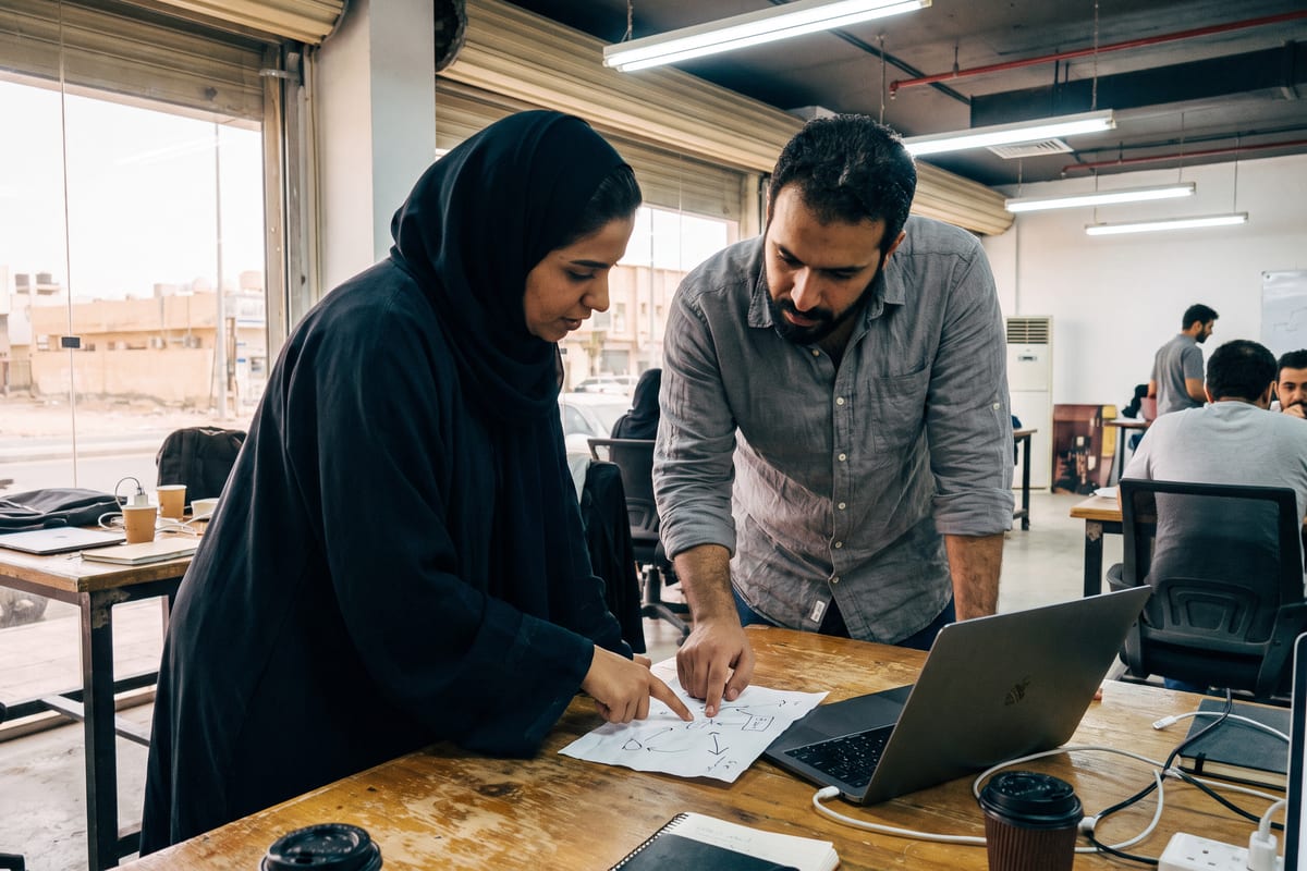 A small team in a Riyadh co-working space maps out an AI automation workflow on paper, mid-discussion.