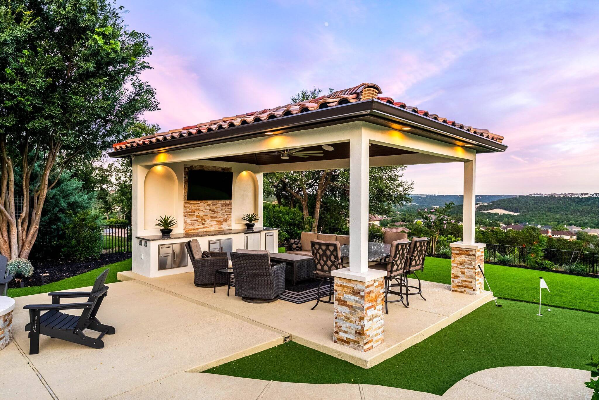 AI patio design example showing luxury outdoor kitchen with pergola, stone columns, and dining area overlooking landscaped backyard